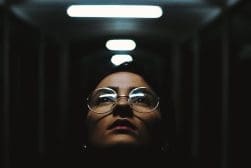A woman in glasses standing in a dark hallway.