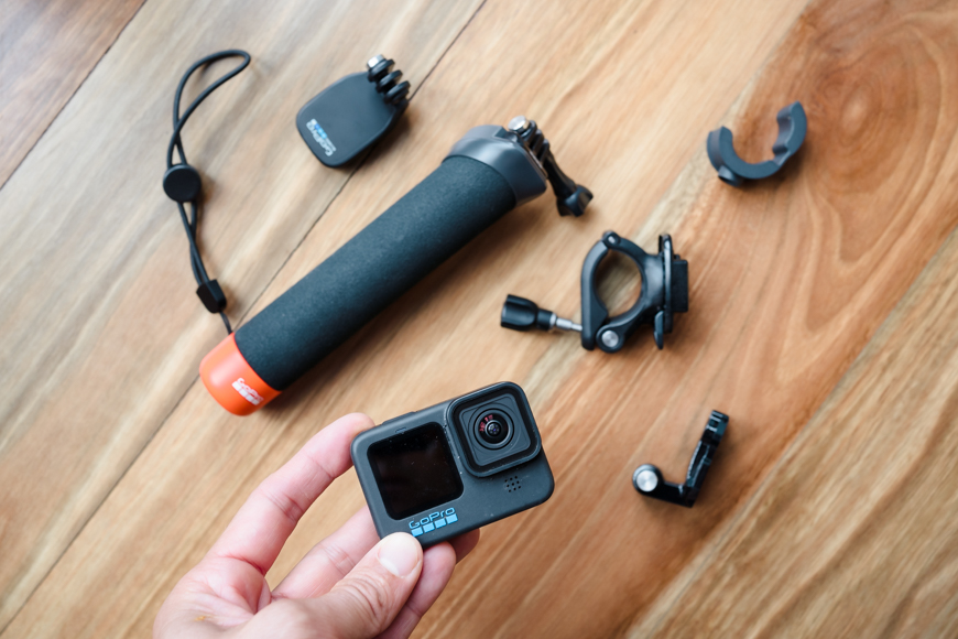 A person holding a gopro and other accessories on a wooden floor.