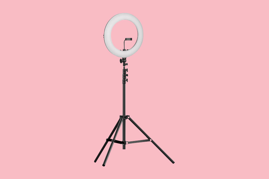 A ring light on a tripod against a pink background.