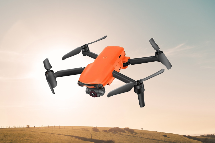 An orange drone flying over a field.