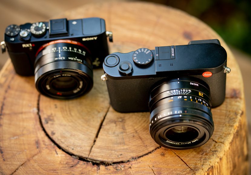 two compact cameras sitting on a wooden stump.