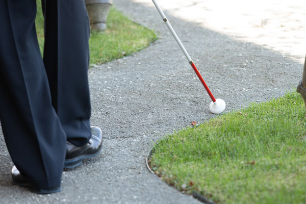 Man learns how to use his white cane on a winding path outdoors.