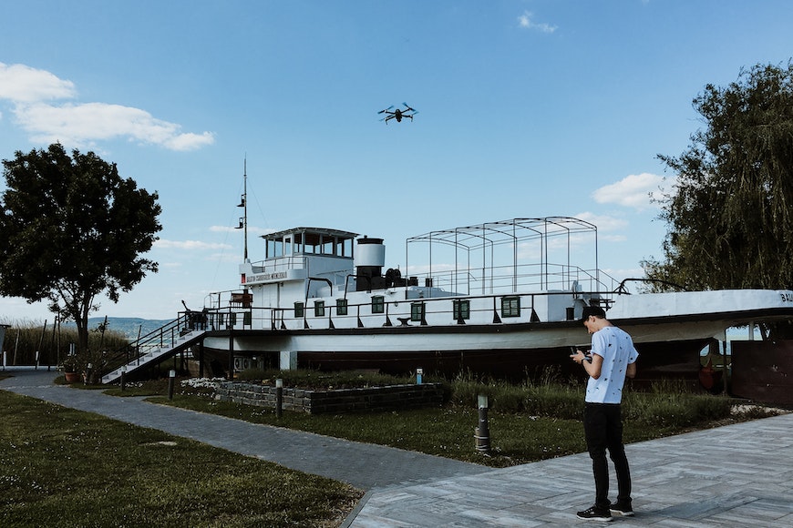 a man standing in front of a boat with a drone flying over it.