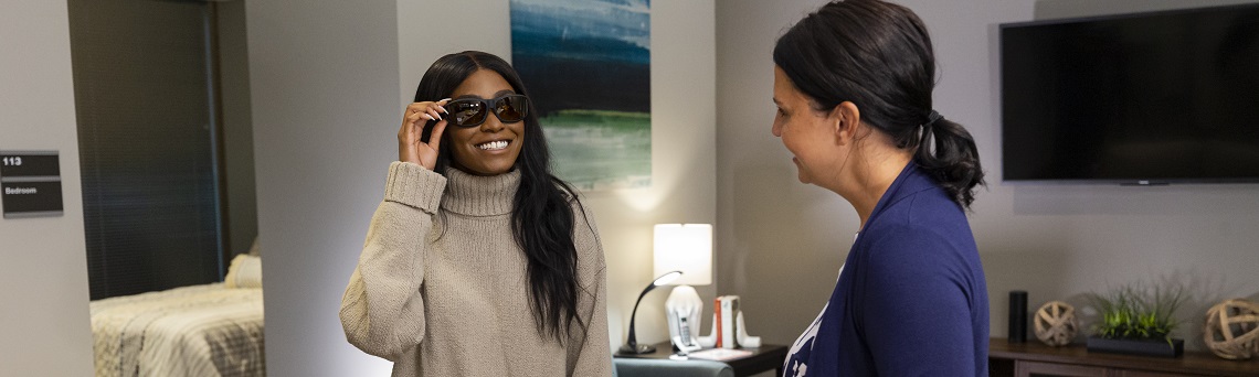 Two women in Envision Dallas's Esther's Place model apartment trying on low vision adaptive devices