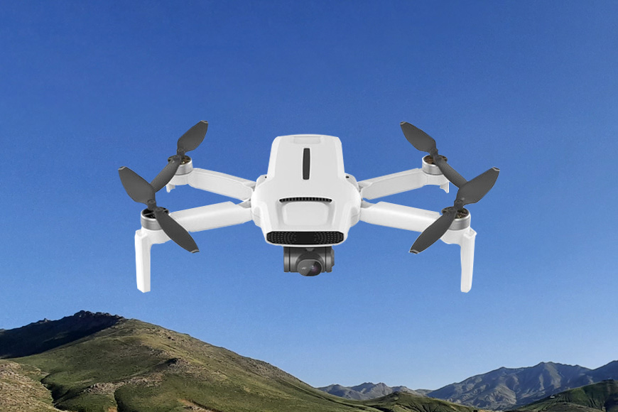 A white dji drone flying over a mountain.