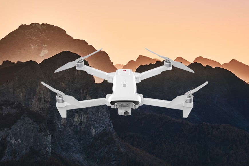 A white drone flying over a mountain at sunset.