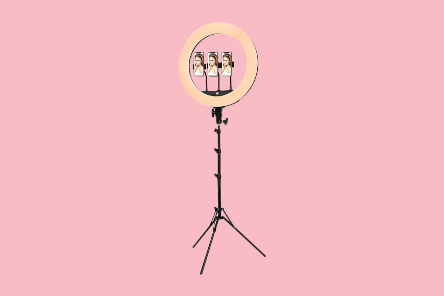 A ring light on a tripod with a pink background.