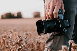a man holding a camera in a field of wheat.