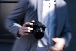 a man in a suit and tie holding a Fujifilm gfx100s camera with lens attached.