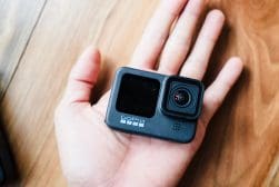 A person's hand holding a small black gopro camera.