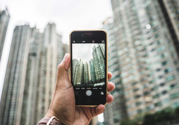 A person is taking a picture of a building with tall buildings in the background.