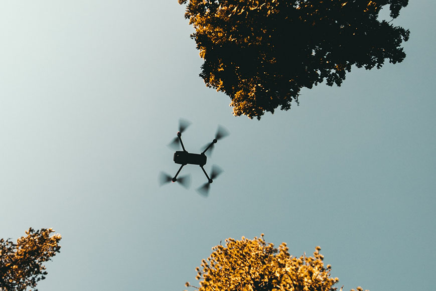 A drone flying in the sky with trees in the background.