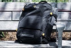 A black backpack sits on a wooden bench.