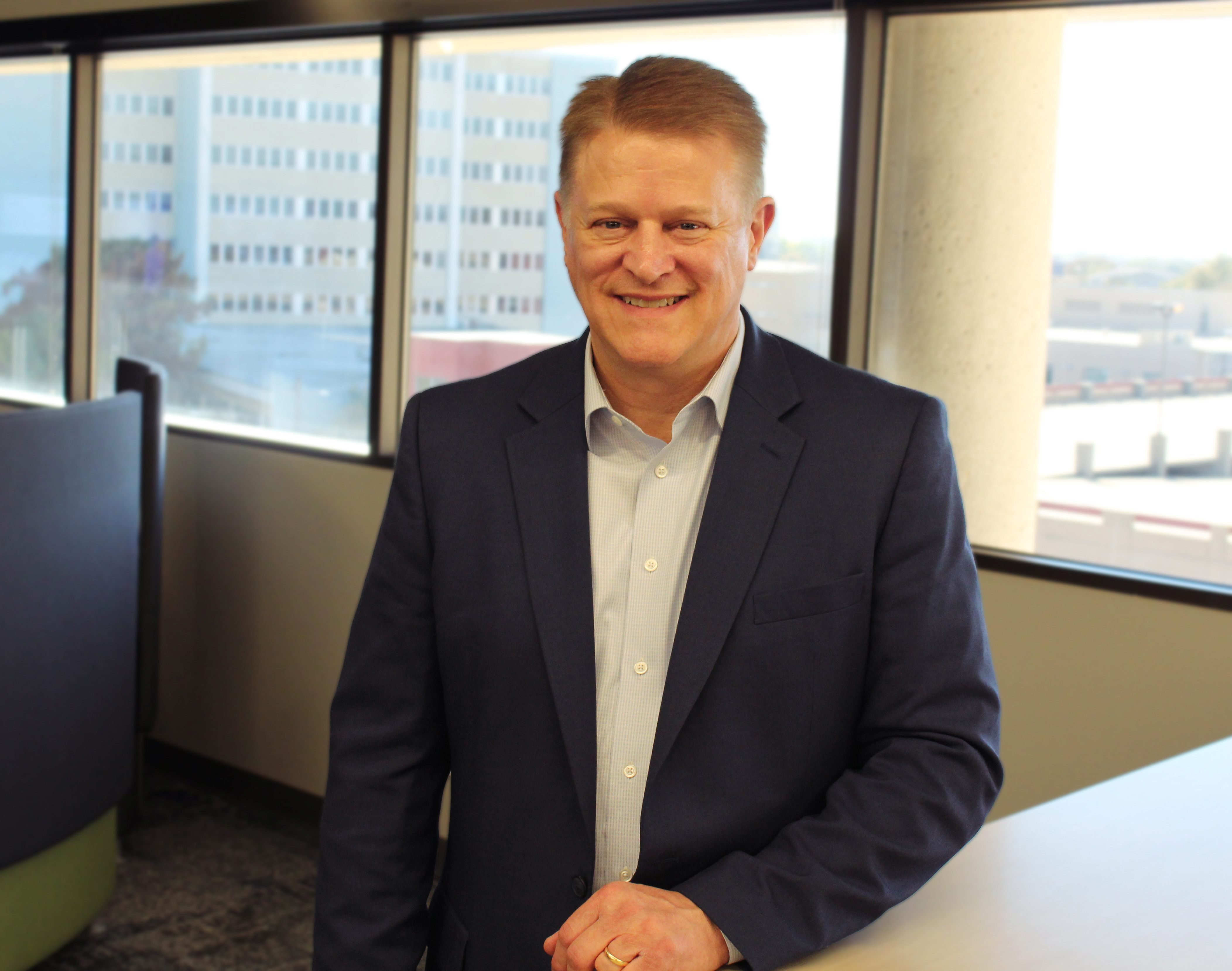 Patrick Tuttle standing next to windows showing the city building in Wichita