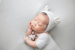 A baby sleeping in a white outfit with a teddy bear.