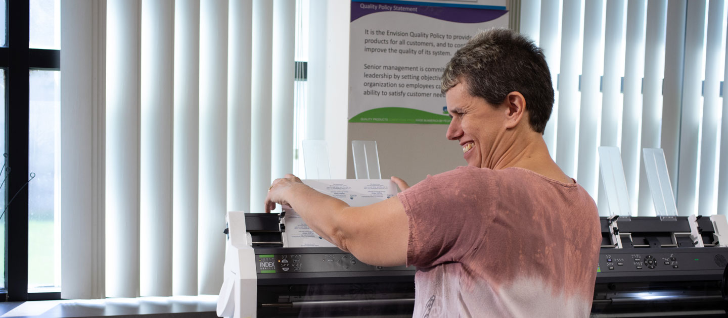 Employee who is visually impaired places business cards into the brailing machine at the Envision Print Shop.