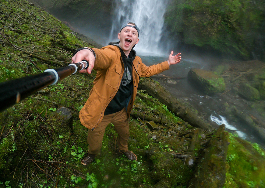 A man is taking a selfie in front of a waterfall.