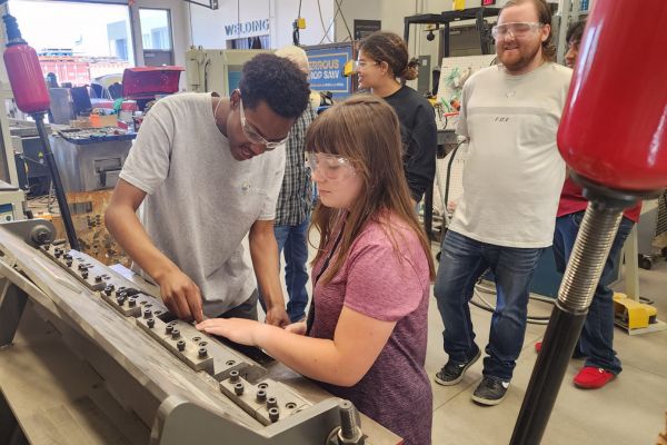 A young visually impaired girl being shown how to feel for mechanical parts inside the GoCreate welding shop.