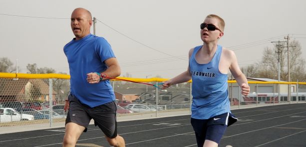 Caleb and his running guide Greg on the track together running, a band holding their wrists together.