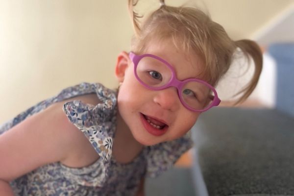 Charlotte wearing pink glasses with her hair styled in two pigtails, her face close up to the camera and she laughs while looking at the camera.