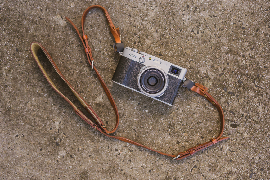 A camera with a leather strap laying on a concrete floor.
