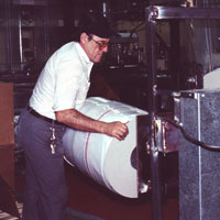 Man who is visually impaired places a roll of plastic on a machine to create plastic bags.