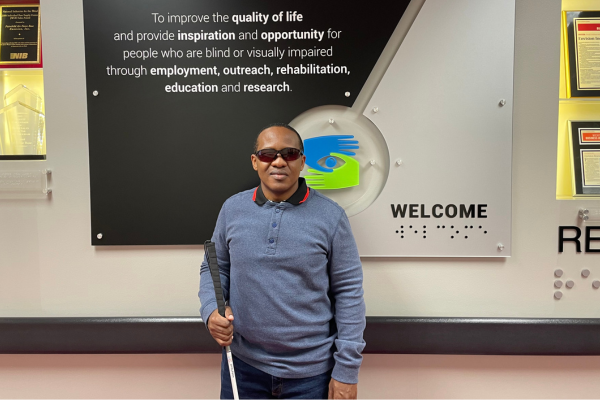 Johnson standing holding his white cane and smiling.